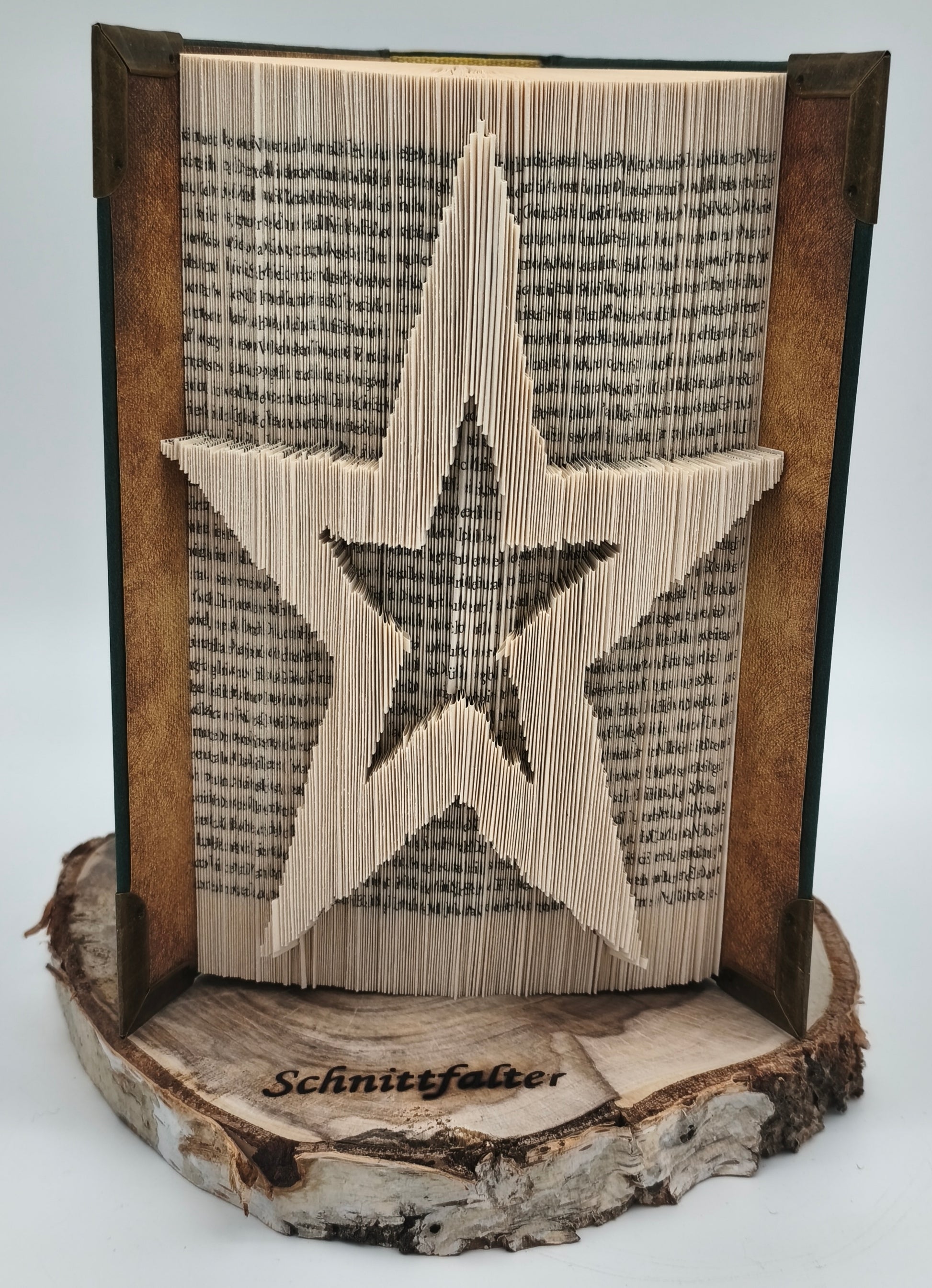 Buchfaltkunst Stern, handgefaltet aus altem Buch auf natürlicher Baumscheibe mit eingebranntem Schnittfalter-Logo, Frontansicht