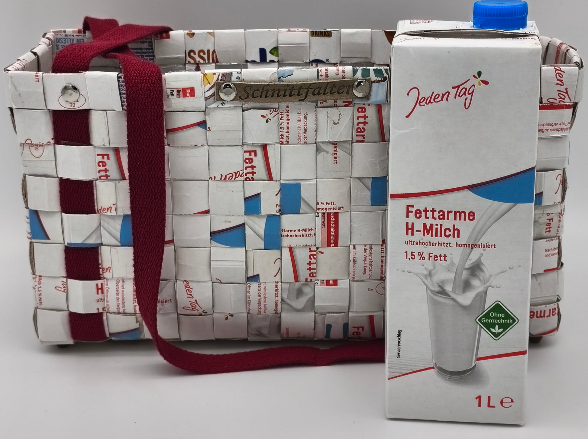 Upcycling Einkaufstasche aus Milch-Tetrapack mit bordeauxrotem Gurtband, Seitenansicht mit Größenvergleich zur 1-Liter-Milchpackung, Schnittfalter-Label sichtbar