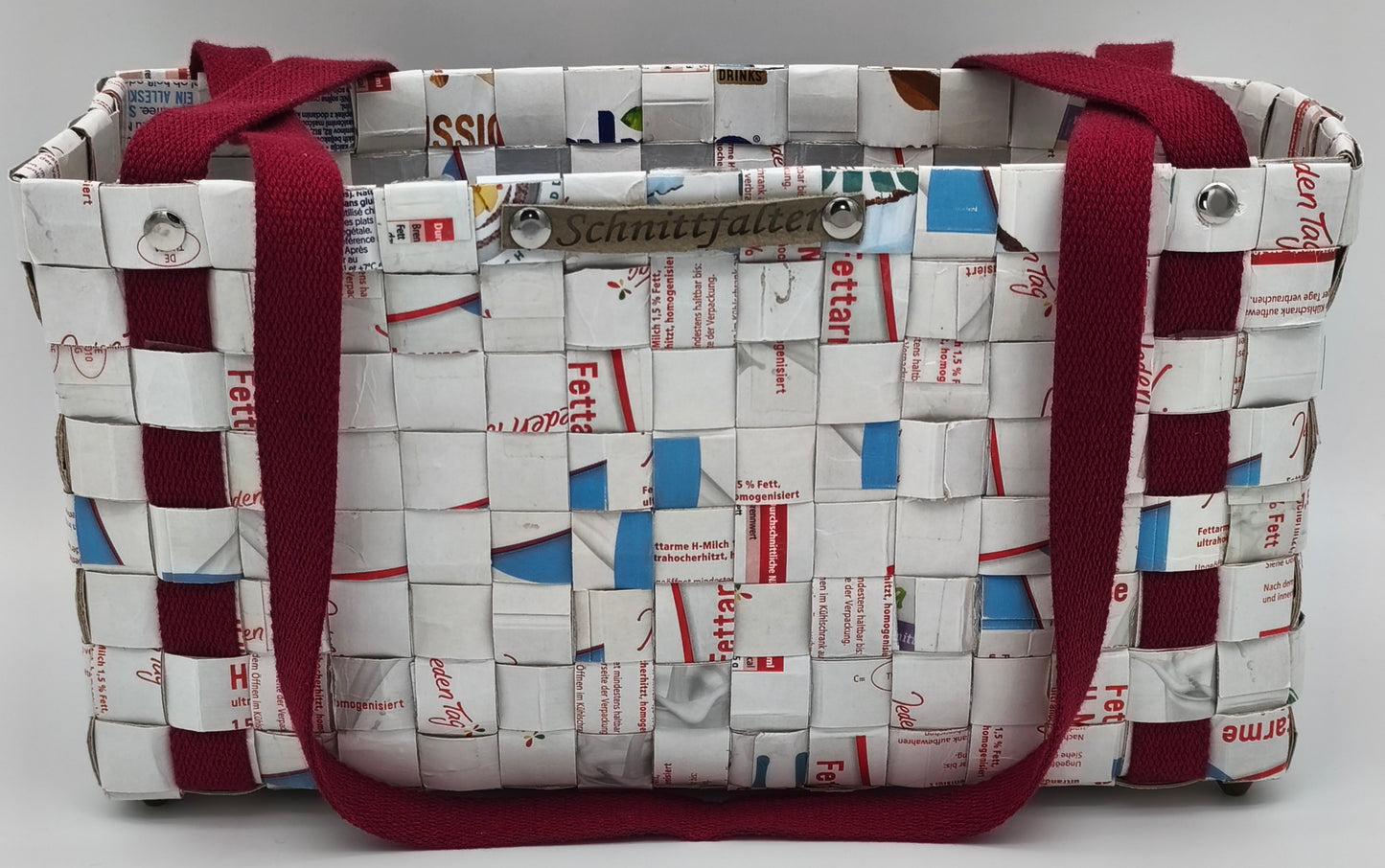 Upcycling Einkaufstasche aus Milch-Tetrapack, Frontansicht mit zwei bordeauxroten Tragegriffen und Schnittfalter-Label
