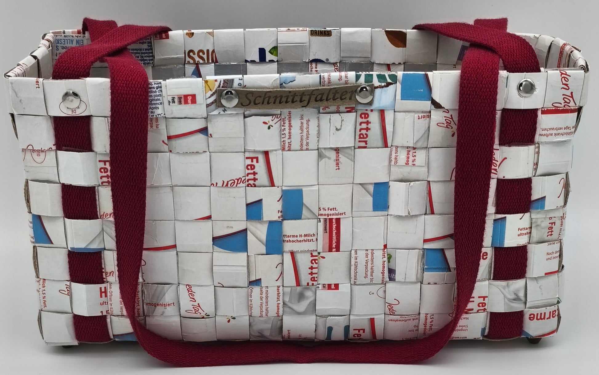 Upcycling Einkaufstasche aus Milch-Tetrapack, Frontansicht mit zwei bordeauxroten Tragegriffen und Schnittfalter-Label