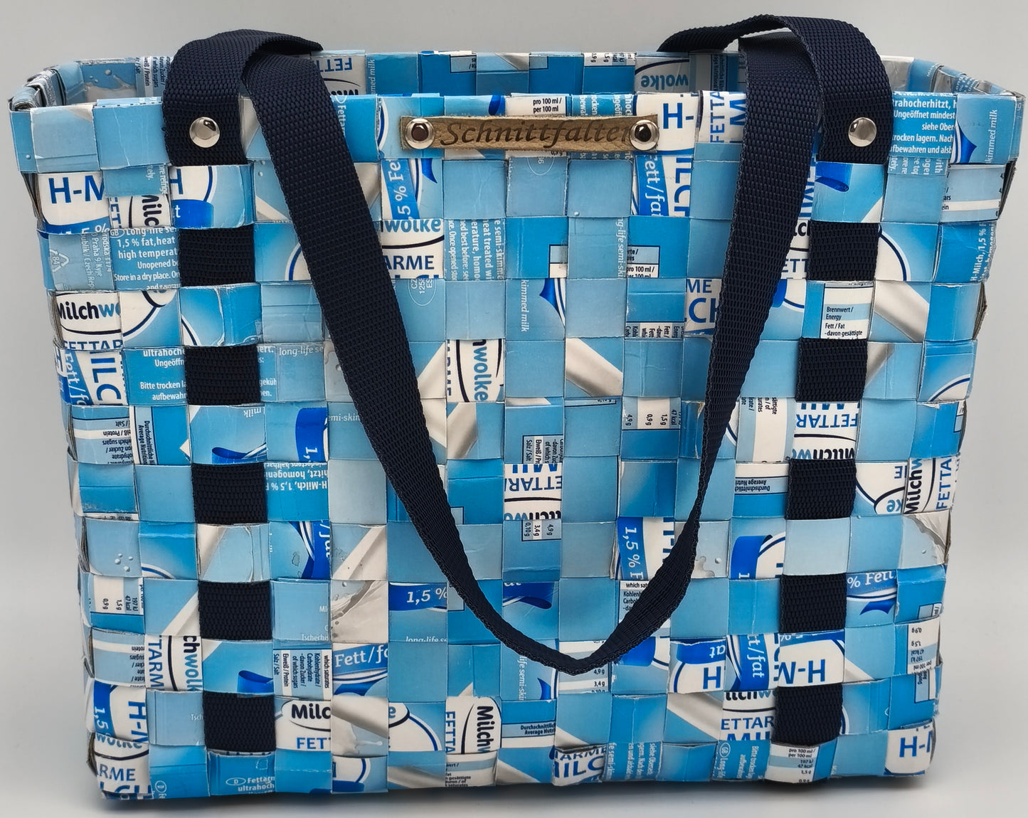 
Upcycling Einkaufstasche Hellblau-Weiß aus Milch-Tetrapack, Frontansicht mit blauem Gurtband, Schrauben und Schnittfalter-Label