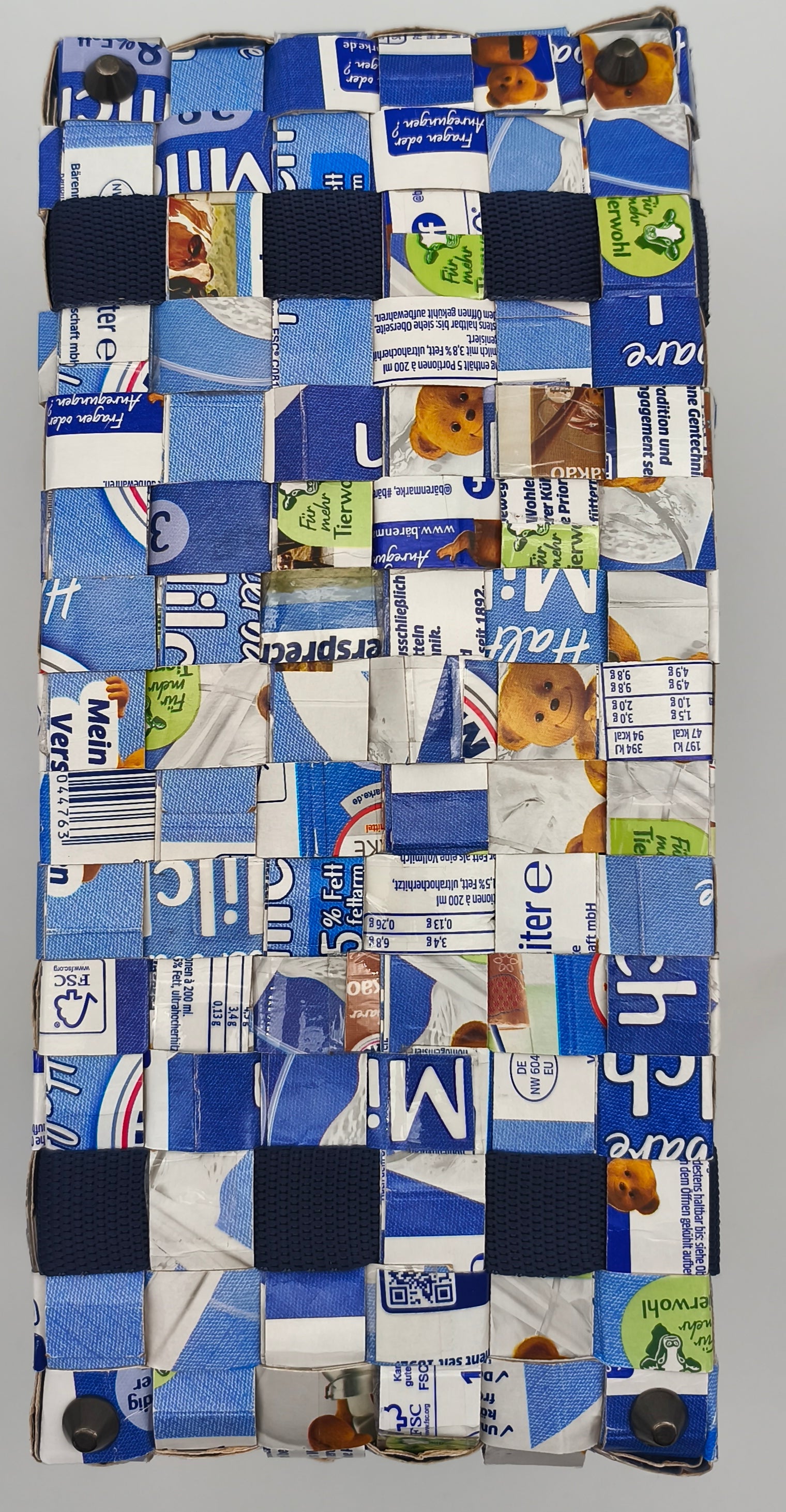 Bodenansicht der handgefertigten Milch Tetrapack Tasche, gewebtes Muster in Blau-Weiß mit dunkelblauen Gurtband Elementen und Taschenfüßen an den Ecken